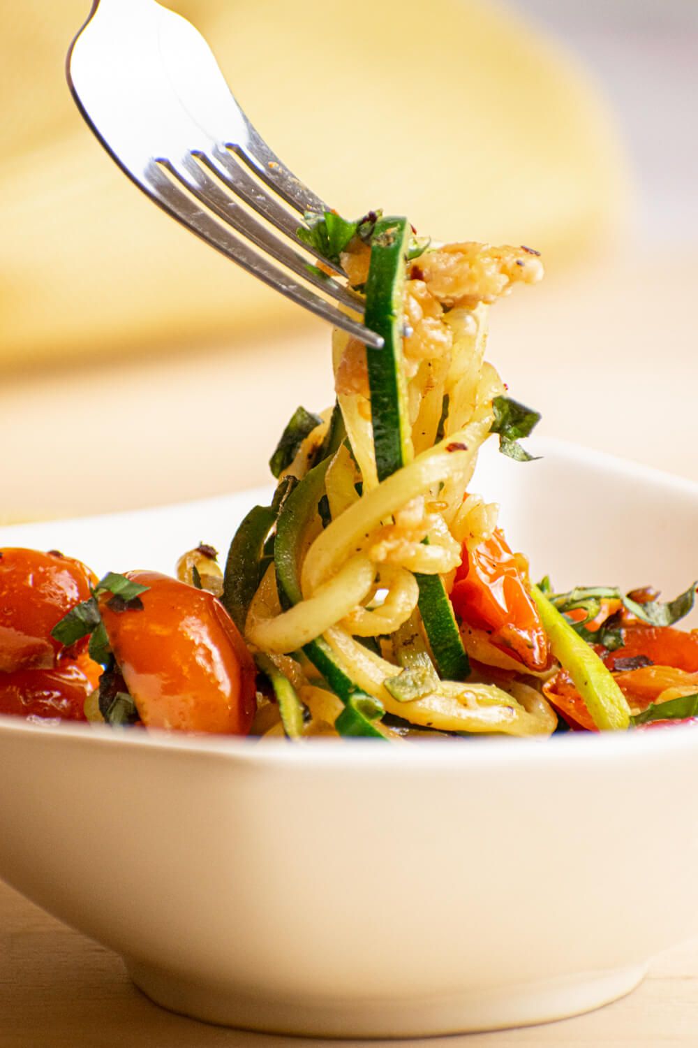 Zucchini noodles with cherry tomatoes, sausage, and garlic in a bowl with a fork.