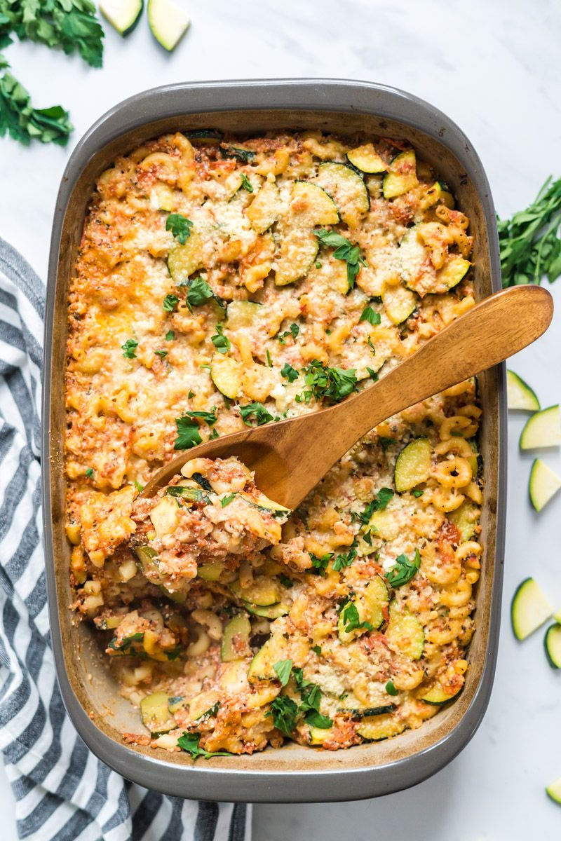 Baked zucchini pasta with ricotta and parmesan cheese in a baking dish with herbs on the side.