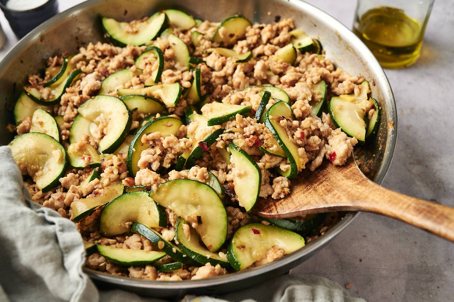 Skillet filled with ground turkey and zucchini stir fry, with a wooden spoon scooping up the mixture.