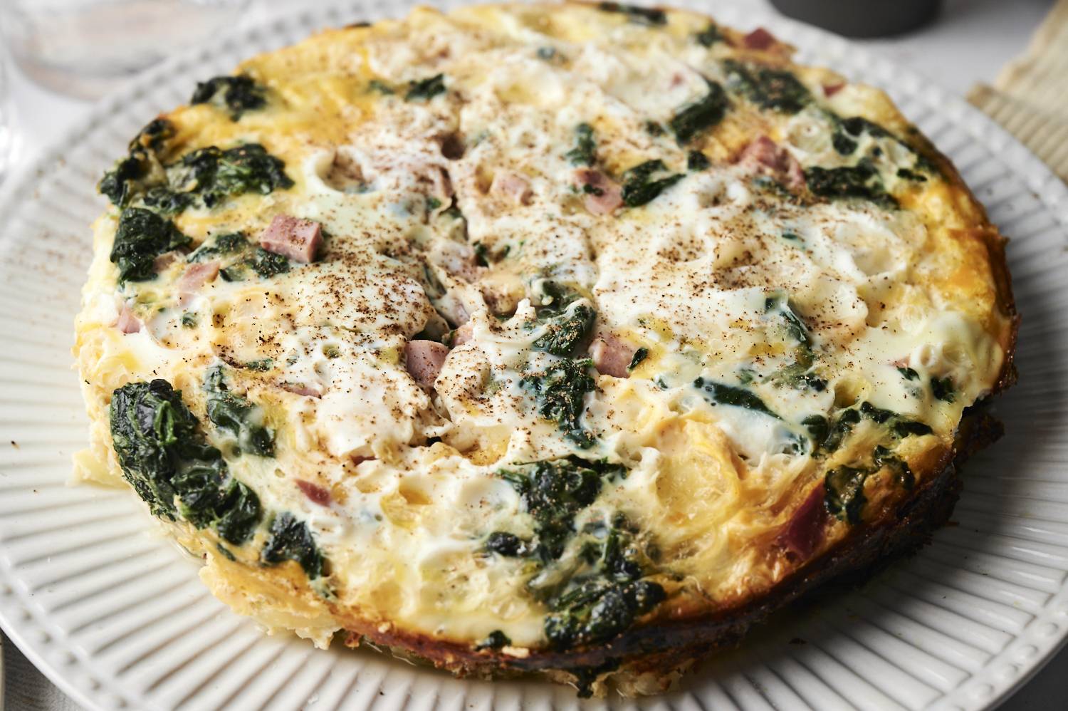 A side view of the whole breakfast casserole on a plate, highlighting the golden edges, creamy egg texture, and seasoned top.