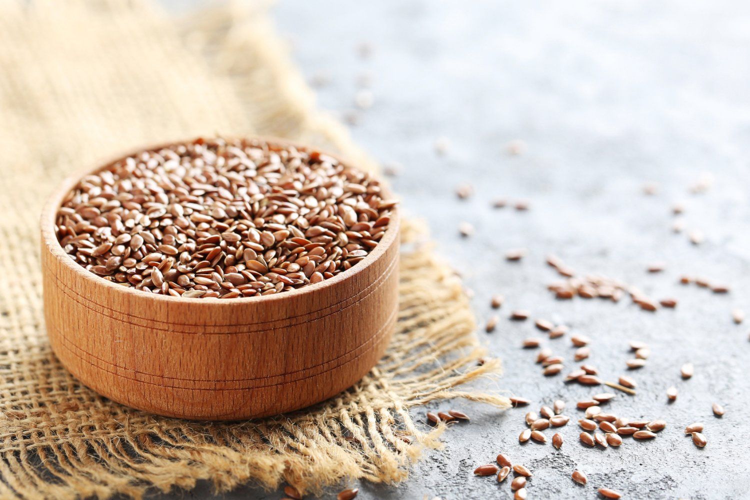 Flaxseed: The Nutrient Packed Seed You Should Eat A bowl of flaxseeds on a burlap napkin with some loose flax seeds.