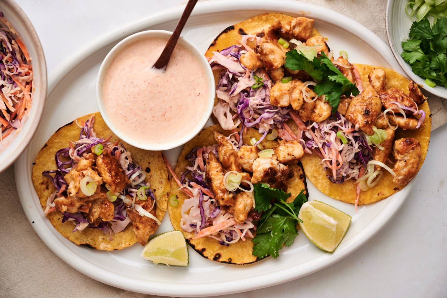Bang Bang Chicken Tacos Bang bang chicken tacos served on warm corn tortilla with crunchy cabbage slaw, cilantro, lime wedges, and green onions.
