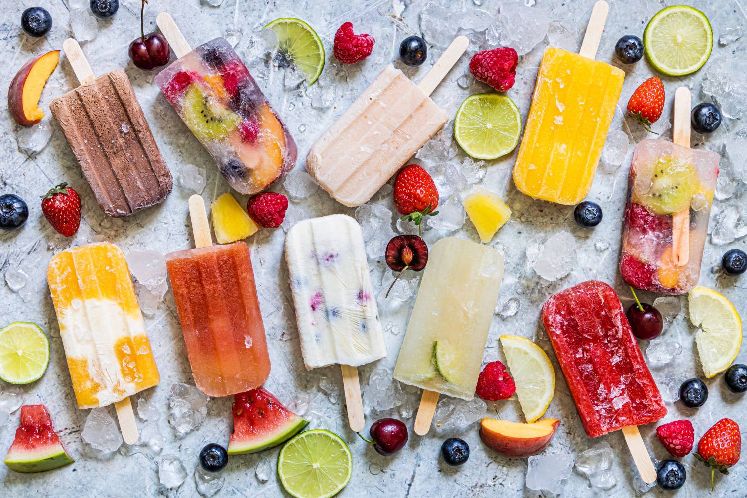 Homemade Fruit Popsicles Fruit popsicles on a marble board with ice and fresh fruit.