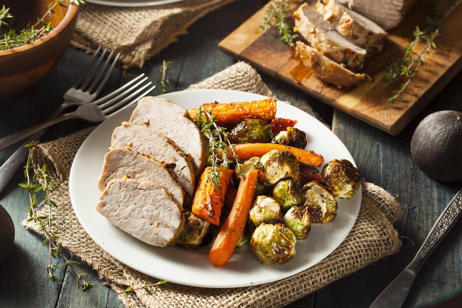 Slow Cooker Thanksgiving Recipes Slow Cooker Maple Pork Tenderloin sliced on a plate with carrots and Brussels sprouts.