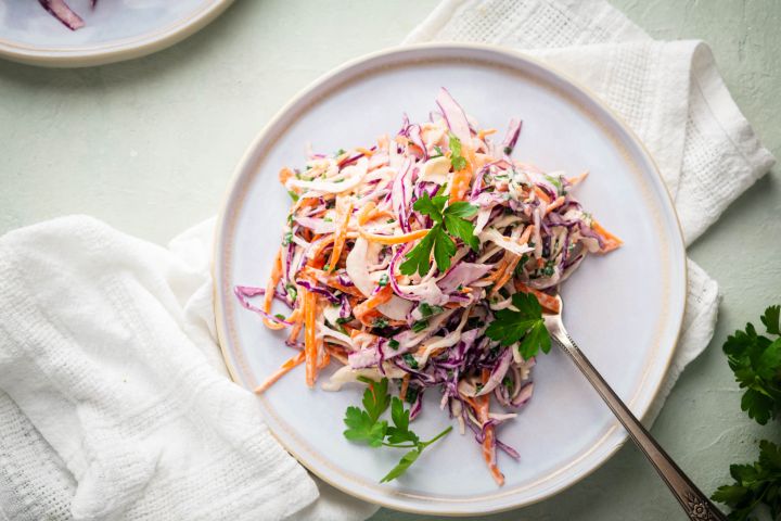 The Best Coleslaw (with Greek Yogurt!) Coleslaw with shredded purple cabbage, green cabbage, carrots, and cilantro on a white plate.