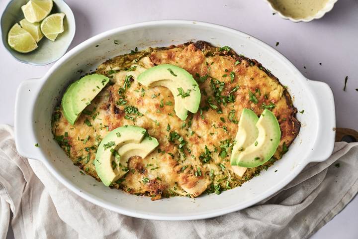 Enchiladas Suizas A freshly baked dish of enchiladas topped with avocado slices, sour cream, cilantro, and seasoning.