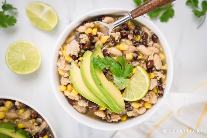 Green Turkey Chili (Shortcut) Green turkey chili with ground turkey, black beans, white beans, corn, and sliced avocado in a bowl.