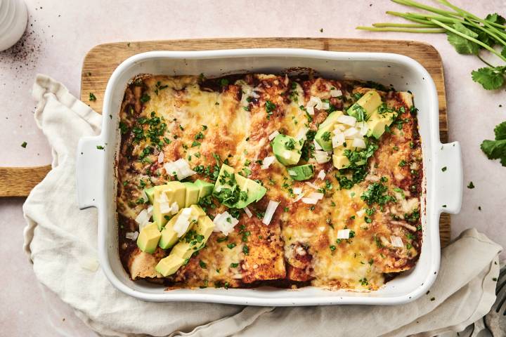 Ground Turkey Enchiladas A savory enchilada filled with beans and chicken, topped with avocado, onion, and cilantro sits on a white plate.
