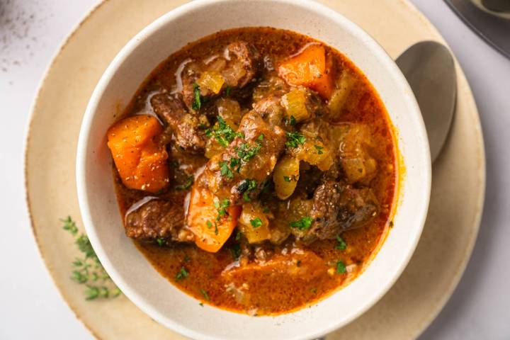 Healthy Instant Pot Beef Stew (or Slow Cooker) A bowl of hearty beef stew with chunks of carrot, celery, and garnished with fresh parsley, served on a cream-colored plate.