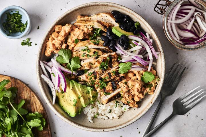 Mexican Street Corn Chicken Bowl A bowl filled with grilled chicken, rice, black beans, avocado, red onion, and creamy sauce, garnished with fresh cilantro.