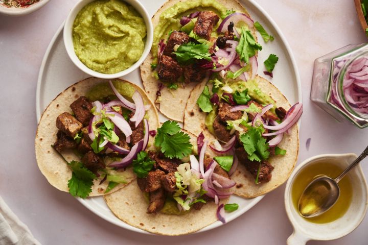 Pork Tacos Pork tacos with crispy pork, red onions, cilantro, and avocado on a plate.