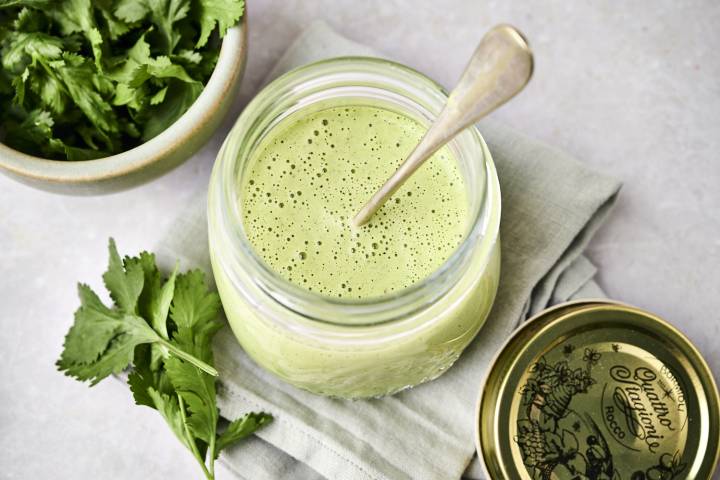 Roasted Poblano Crema A jar of green smoothie with bubbles and a spoon, beside a bowl of fresh cilantro on a cloth.