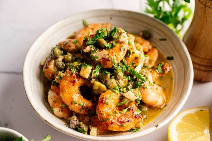 Shrimp Piccata A bowl of golden-brown shrimp coated in a lemony garlic butter sauce, garnished with capers and fresh herbs. The setting conveys a fresh, appetizing tone.