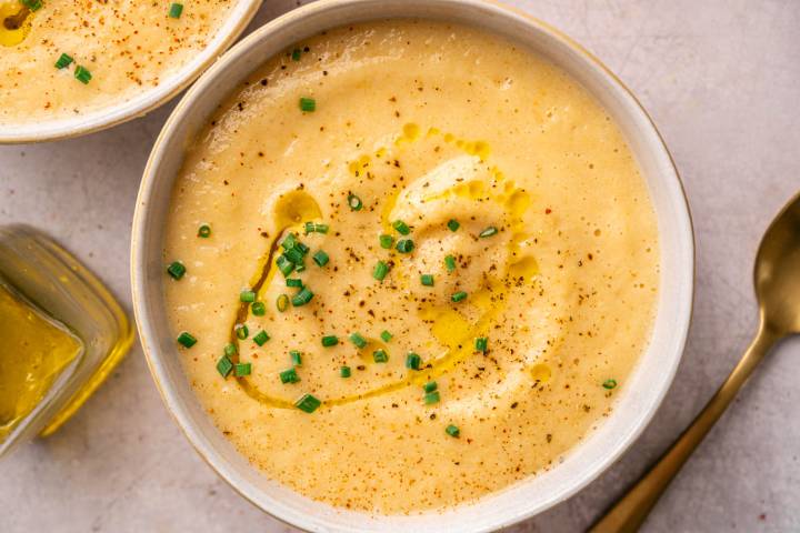 Slow Cooker Cheesy Cauliflower Soup A creamy bowl of potato soup garnished with chopped chives and a drizzle of olive oil, with a sprinkle of black pepper.