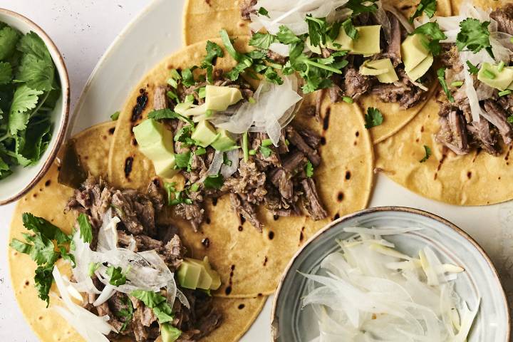 Slow Cooker Salsa Verde Beef Shredded salsa verde beef served in corn tortillas, garnished with chopped onions, sauce, and fresh cilantro.