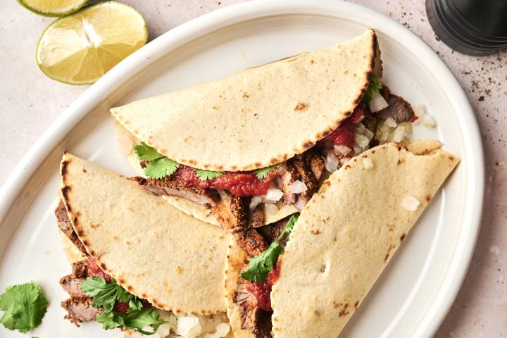 Steak Tacos Overhead view of assembled steak tacos filled with grilled beef, onions, salsa, and fresh cilantro on a white oval platter.