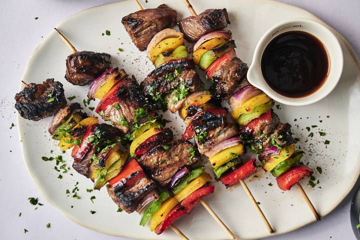 Teriyaki Beef Kabobs Grilled kebabs featuring marinated beef and colorful vegetables, served with a small bowl of dipping sauce on a white plate.