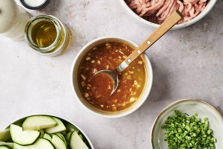 Ground Turkey and Zucchini Stir Fry Bowl of homemade stir-fry sauce with garlic, ginger, and seasonings, surrounded by raw ground turkey, chopped zucchini, and green onions on a kitchen counter.