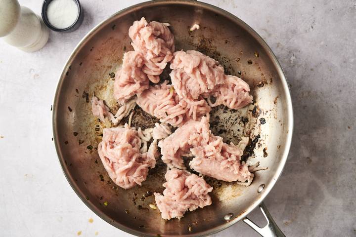 Ground Turkey and Zucchini Stir Fry Raw ground turkey added to a skillet, beginning to cook with browned bits and aromatics on the pan.