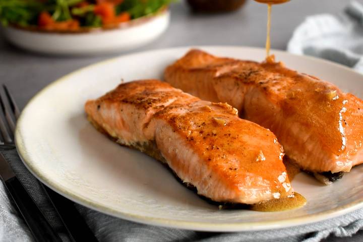 Pan Seared Salmon Garlic lemon butter sauce being poured over salmon on a plate.