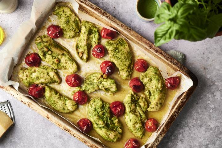 Pesto Chicken Sheet pan filled with baked pesto-coated chicken and blistered cherry tomatoes, fresh from the oven and ready to serve.