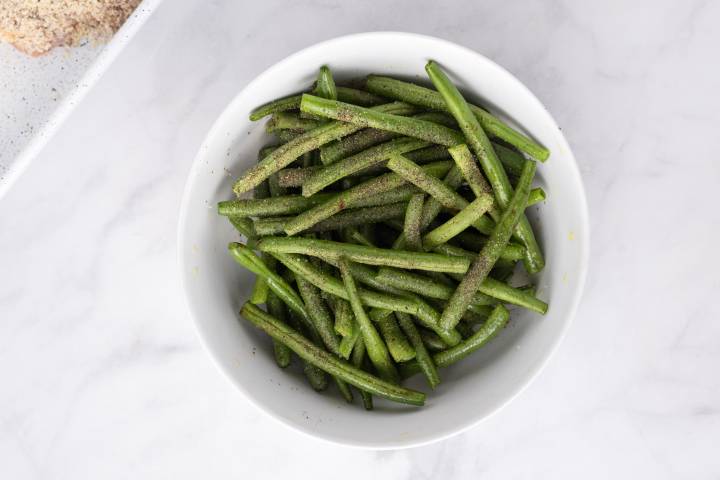 Sheet Pan Healthy Chicken Parm Green beans being tossed with olive oil, salt, and pepper.
