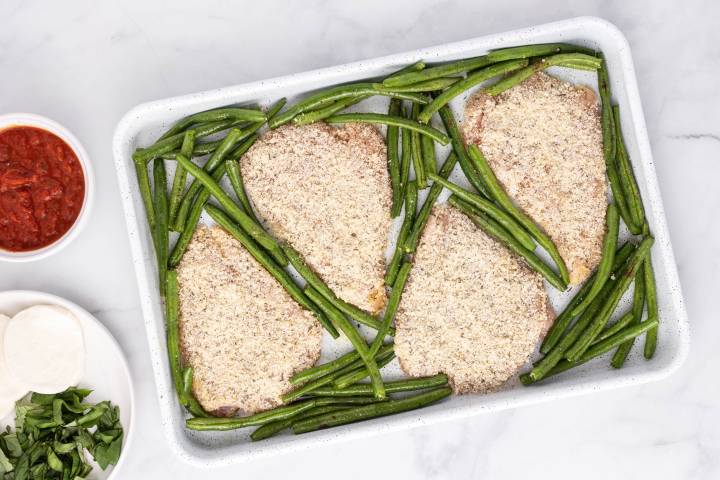Sheet Pan Healthy Chicken Parm Breaded chicken breast and green beans on a baking sheet.