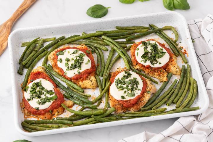 Sheet Pan Healthy Chicken Parm Baked chicken parmesan with green beans on a baking sheet.