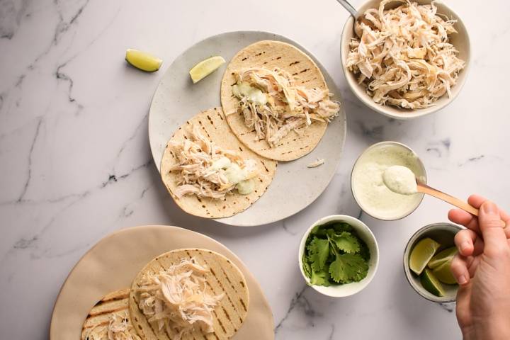 Slow Cooker Jalapeno Chicken Tacos Cilantro yogurt sauce being spooned over shredded jalapeno chicken.