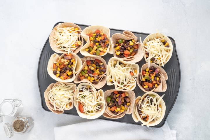 Taco Cups Tortilla cups in a muffin tin filled with bean taco filling and shredded cheese.