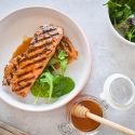Grilled Salmon With Honey & Lime Grilled honey and lime salmon on a plate with sauce and a salad on the side.