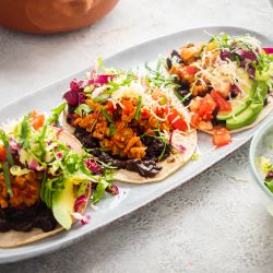 Easy Ground Beef Tostadas Beef tostadas with ground beef, refried beans, avocado, salsa, lettuce, tomato, and cheese on a plate.