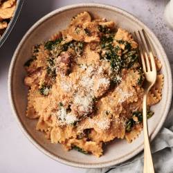 Easy High Protein Pasta Creamy high-protein pasta made with bowtie noodles, sausage, spinach, and ricotta, served in a beige bowl and topped with grated Parmesan cheese. A gold fork rests on the side.