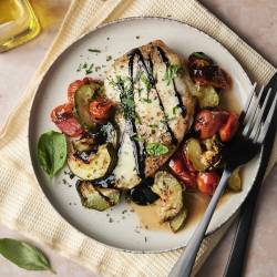 Sheet Pan Caprese Chicken A plate of caprese chicken with roasted zucchini and tomatoes, topped with balsamic glaze and fresh basil.