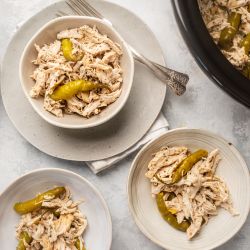 Slow Cooker Pepperoncini Chicken Slow cooker pepperoncini chicken shredded in three bowls with rice on the side and whole pepperoncini peppers.