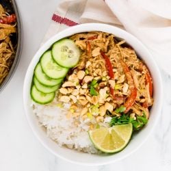 Slow Cooker Thai Peanut Chicken Slow Cooker Thai Peanut Chicken in a bowl with rice, cucumbers, chopped peanuts, and lime.