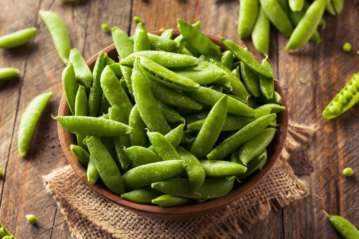The Ultimate Guide to Snap Peas Raw sugar snap peas ion a bowl on a wooden countertop.