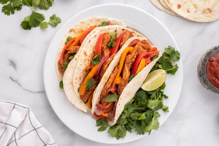 The Best Fajita Toppings Chicken fajitas topped with peppers, onions, cilantro, and lime in flour tortillas.