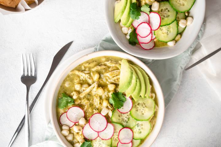 16 Cozy Mexican Soup Recipes Green chicken pozole in a bowl with avocado, radish, cilantro, chicken, and hominy.