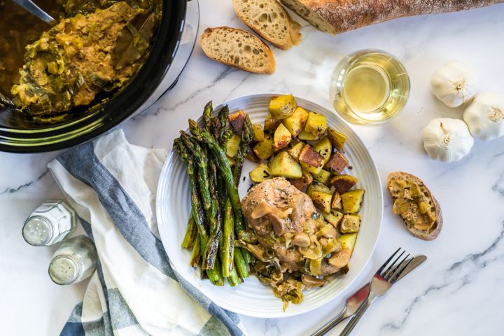 40 Clove of Garlic Chicken (Slow Cooker) Forty clove of garlic chicken breasts cooked with whole garlic cloves and leeks on a plate with roasted potatoes and asparagus.