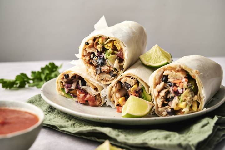 Fish Burritos A plate of fresh and flavorful Fish Burritos, packed with black beans, corn, avocado, cabbage slaw, and juicy seasoned fish, wrapped in soft tortillas and served with lime wedges.