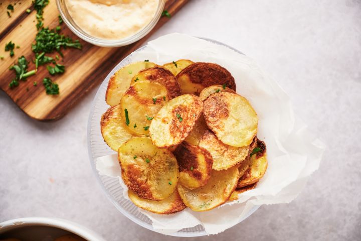 Baked Potato Chips Baked potato chips on parchment paper with with parsley and dipping sauce.