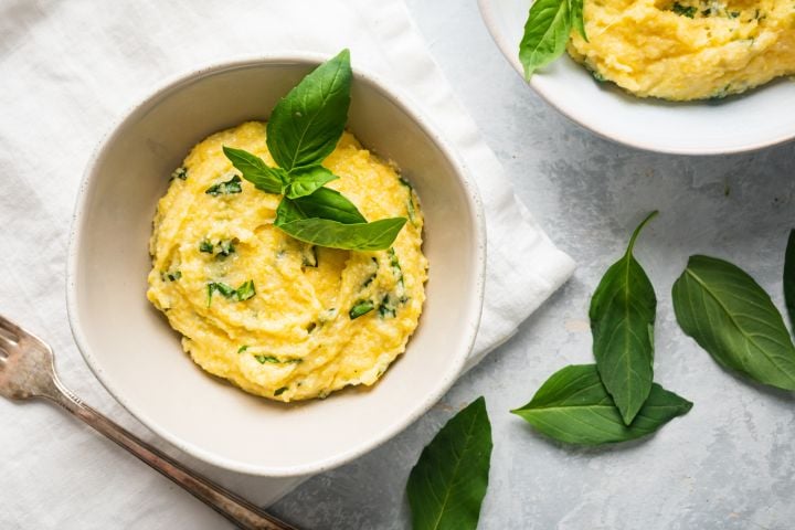 Parmesan Polenta with Basil Basil Parmesan polenta in a bowl with fresh basil leaves on top.