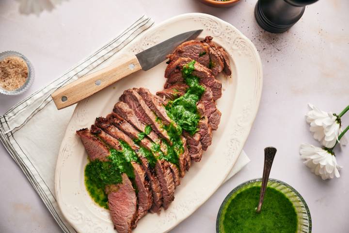 Broiled Flank Steak Broiled flank steak cooked until medium rare and sliced on a plate with chimichurri.