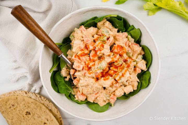 Buffalo Chicken Salad Buffalo chicken salad with fresh spinach, a whole wheat wrap, and a spoon in a bowl.