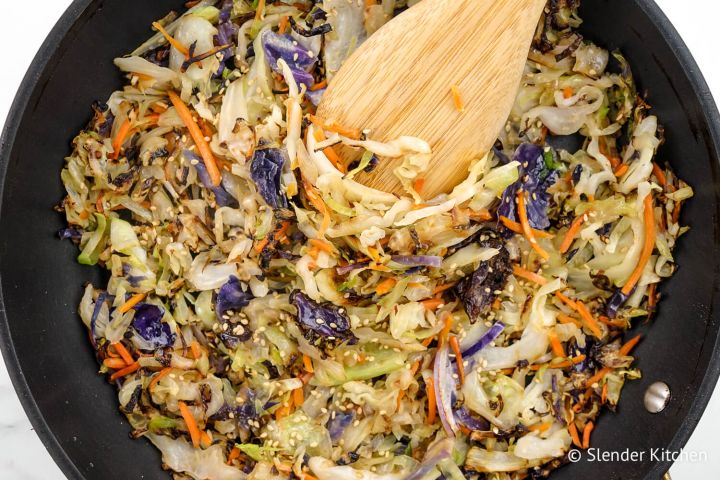 10 Minute Cabbage Stir Fry Cabbage stir fry in a black skillet with sliced green cabbage, carrots, and soy sauce.