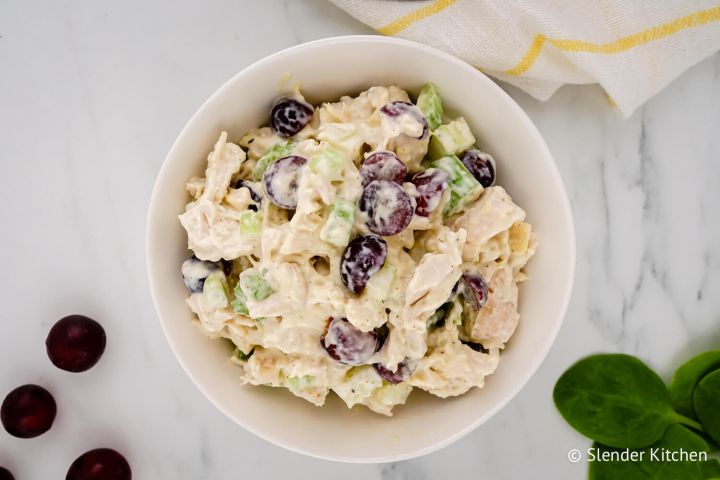 Healthy Chicken Salad with Grapes Chicken salad with grapes, celery, and yogurt dressing in a bowl with grapes and spinach on the side.