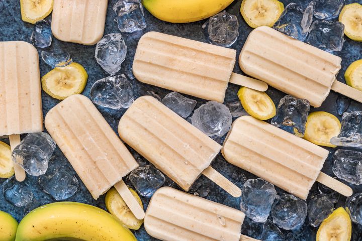 Creamy Banana Popsicles Banana popsicles with blended fresh bananas, yogurt, and honey on a marble board with banana slices.