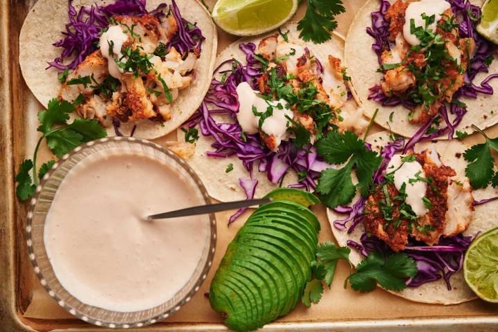 Fish Taco Sauce Fish taco sauce in a bowl and served drizzled over fish tacos with cabbage, cilantro, and avocado.