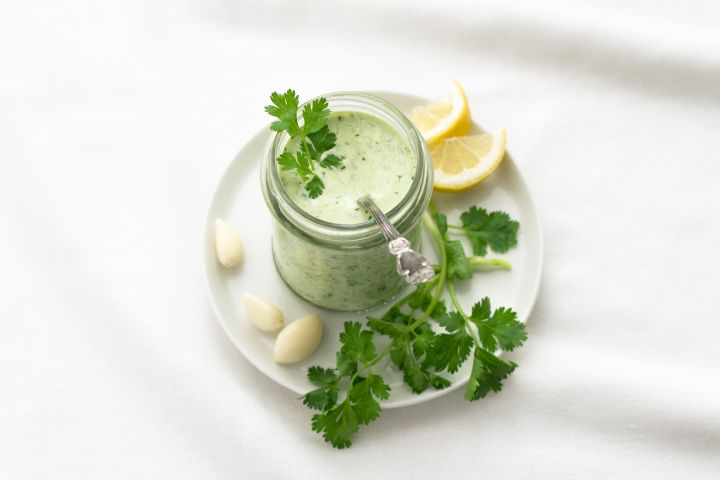 Homemade Green Goddess Dressing Green goddess dressing in a glass jar with fresh cilantro, garlic, and lemon on the side.